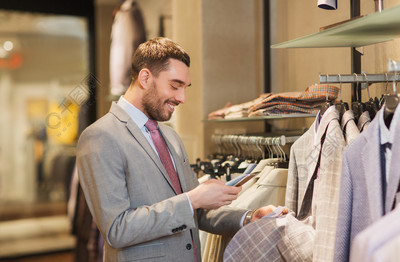 销售,购物,时尚,技术和人的概念- -快乐的人,穿着与智能手机在服装店选择衣服